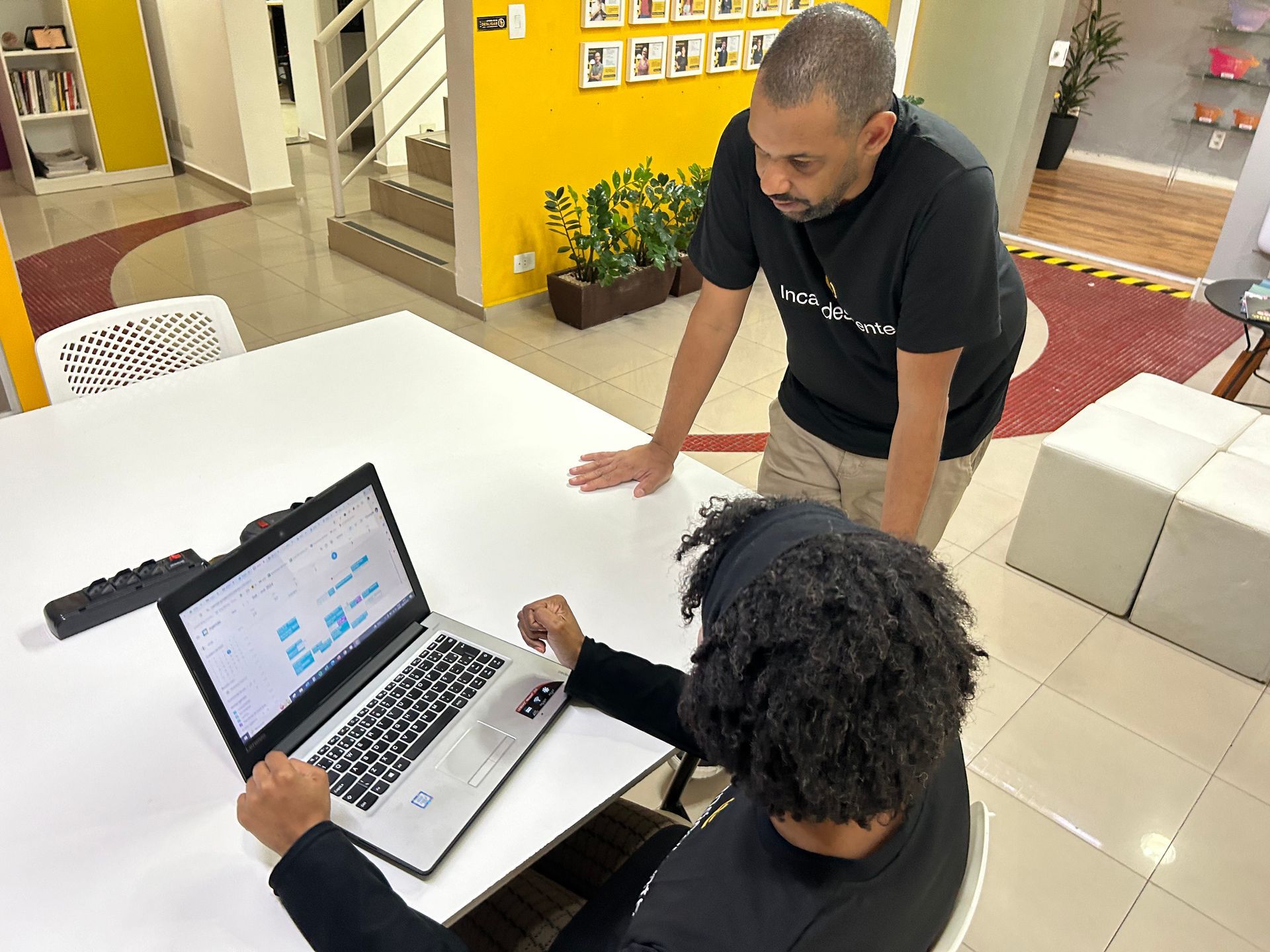 Um homem está de pé ao lado de uma mulher usando um laptop.