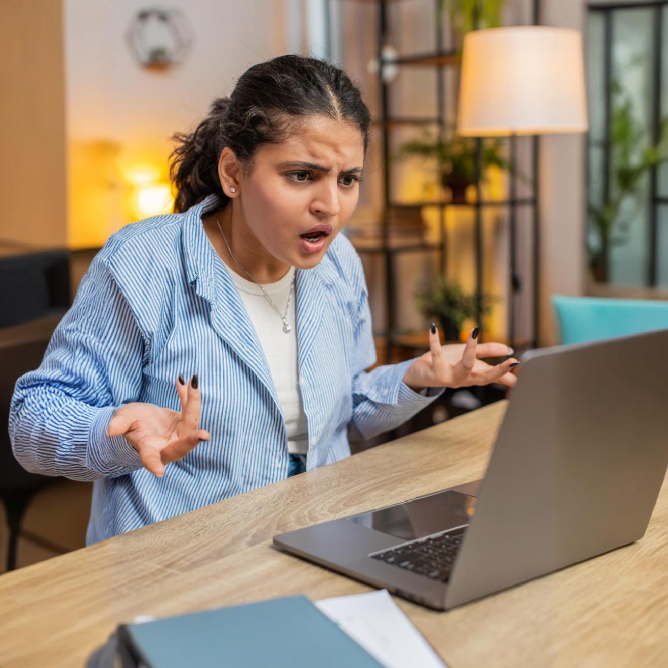 mulher branca olhando para a tela de notebook com indignação