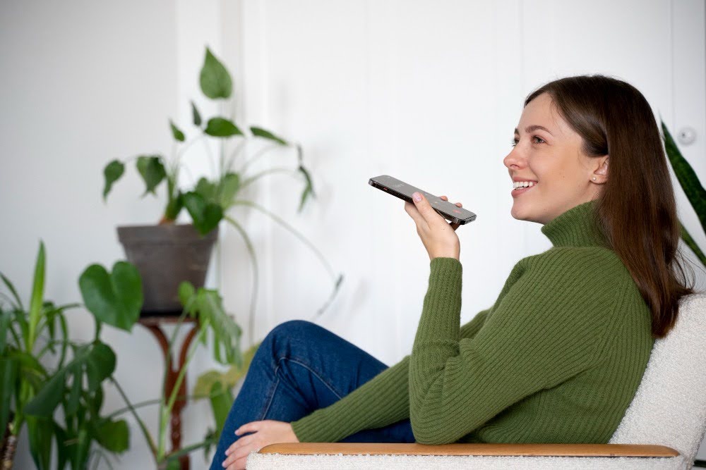 mulher sentada no sofá usando o recurso de voz do celular