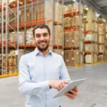 homem brando em um armazém sorrindo e segurando um tablet.