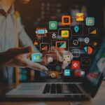 notebook aberto sobre a mesa e ícones de marketing saltando da tela.