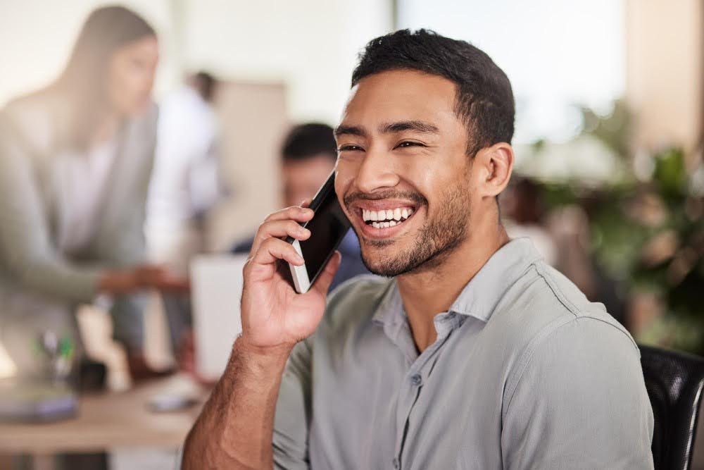 homem branco sentado sorrindo e falando ao telefone