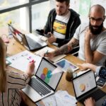 profissionais com notebooks sentados em uma mesa retangular