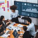 profissionais debatendo sobre dashboards que estão na mesa e no telão